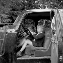 Boy sitting at the wheel of a broken car, adventure playground Ruschlikon 1954