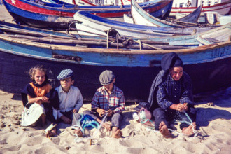 Fisherman and children repairing nets on beach by traditional fishing boats.