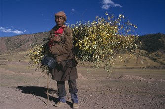 CHINA, Tibet, Markam, Man carrying roofing materials on his back