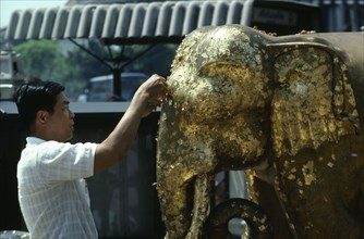 THAILAND, Bangkok, Man attaching gold leafing to an elephant statue at a street temple