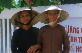 VIETNAM, Danang, "Mother and daughter standing with linked arms, wearing traditional straw hats.  "