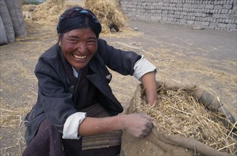CHINA, Tibet, Tandruk, Smiling farm worker with bag of straw.