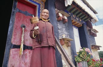 CHINA, Tibet, Samye Monastery, Lama holding prayer wheel outside monastery door.