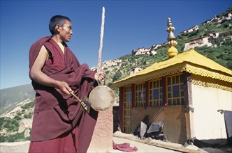 CHINA, Tibet, Drigung Til Monastery, Monk calling other monks to prayer with a drum.