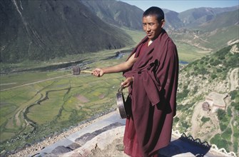 CHINA, Tibet, Drigung Til Monastery, Monk calling others to prayer with drum.