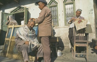 CHINA, Xinjiang Province, Kashgar, Men having their heads shaved by street barbers