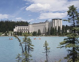 CANADA, Alberta, Lake Louise, Chateau Lake Louise Hotel with canoeists on the tree lined lake