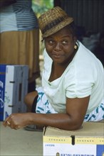 WEST INDIES, St Lucia, Female banana packer wearing hat and leaning on box