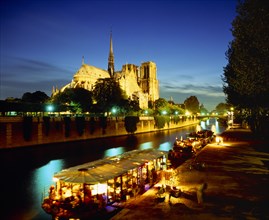 FRANCE, Ile de France, Paris, Notre Dame floodlit at night with restaurant and houseboat lit up on