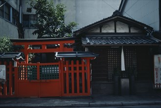 JAPAN, Nara, Exterior of house beside red painted Torii style gateway.