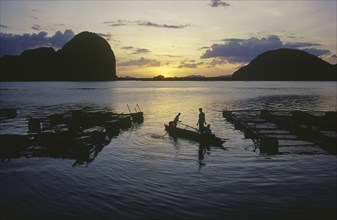 THAILAND, Phang Nga, Fish farm at sunset with two men in a canoe