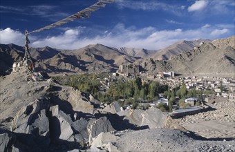 INDIA, Ladakh, Leh, Prayer flags blowing in the wind on top of rocks in the foreground overlooking