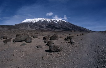 TANZANIA, Kilimanjaro, Snow capped Mount Kilimanjaro with large boulders of rock in the foreground