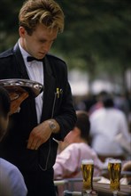 FRANCE, Ile de France, Paris, Formal waiter standing at a table with drinks on and holding a silver