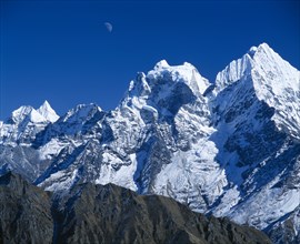 NEPAL, Sagarmatha National Park, Himalayan mountain peaks with moon above just visible in deep blue