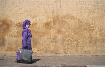 MOROCCO, Traditional Clothing, Woman with veil waliking past colourful wall.
