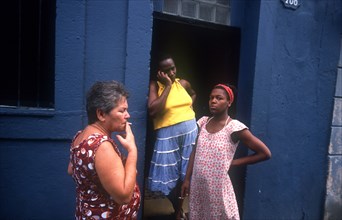 CUBA, Havana, Three women gathered by a doorway of a blue house smoking