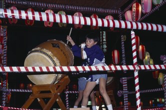 JAPAN, Honshu, Tokyo, Young boy in costume beating a large drum at the O-Bon festival