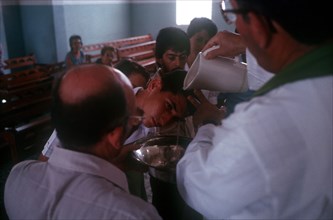 CUBA, Guimero , Man having holy water poured over his head by a priest at an adult Christening