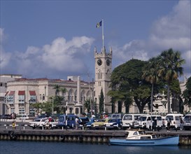 BARBADOS, Bridgetown, The Carenage. Buildings and church clock tower with cars on quay and a boat