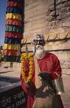 INDIA, Uttar Pradesh, Sarnath, Sadhu holding a trident standing by a stupa