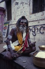 INDIA, Uttar Pradesh, Varanasi, Sadhu sitting cross legged with a bugle in his lap