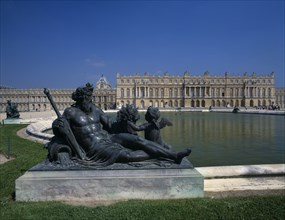 FRANCE, Ile de France, Versailles, Bronze statue beside lake with palace behind and clear blue sky