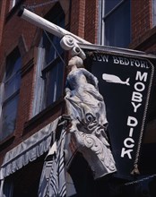 USA, Massachusetts, New Bedford, Moby Dick'hanging sign with ships figurehead on a brick building