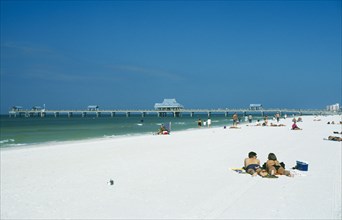 USA, Florida , Clearwater Beach, Sunbathers on white sand beach with pier beyond.