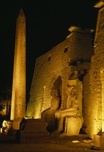 EGYPT, Luxor, The temple illuminated at night seated statues of Ramesses II outside the Pylon with