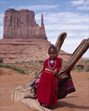 USA, Arizona, Monument Valley, Navejo girl leaning against dead tree wearing a red dress and