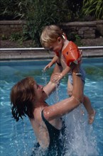 10028042 CHILDREN Leisure Swimming Mother lifting child wearing water wings out of water in swimming pool