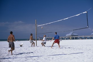 USA, Florida, Clearwater , People playing beach volleyball with small pier in the background