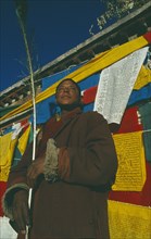 TIBET, Lhasa, Jokhang Temple, Male pilgrim standing outside temple in front of prayer flags
