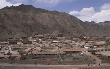 CHINA, Gansu, Xiahe, View over Labrang Monastery surrounded by hills and people walking a path in