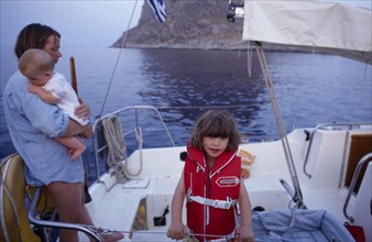 10031034 LEISURE Sailing Yachting Greece. Monemvasia. An English family on a sailing holiday aboard their yacht. Mother holding a baby near a young girl wearing a life jacket