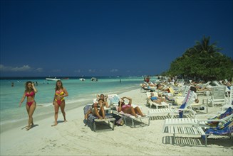 WEST INDIES, Jamaica, Negril, Female tourists beach sunbahing on sun loungers by the water with two