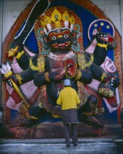 NEPAL, Kathmandu, "Man in front of temple carving of Black Bhairab in Durbar Square depicting Shiva
