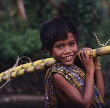 INDONESIA, Lombok, Kuta, Smiling boy with a sarong over his shoulder carrying sugarcane