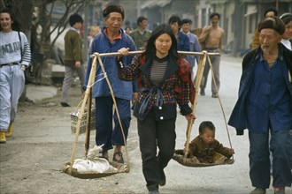CHINA, Guizhou, Bijie, Woman with carrying scales over her shoulders balancing a small child with a