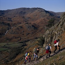 ENGLAND, Cumbria, Lake District, Walkers on footpath to Helm Crag above Grasmere with view west to