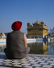 INDIA, Punjab, Amritsar, The Golden Temple.  Man wearing red turban sitting on tiled floor beside