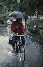 CLIMATE, Rain, Umbrella, Cyclist riding through flooded street holding umbrella with one hand