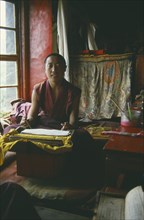 TIBET, Lhasa, Seated monk in room with prayer book