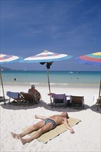 THAILAND, Phuket, Patong Beach, Sun bather lying on the sand in the foreground with row of