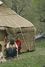 CHINA, Xinjiang, Tianchi, "Kazakh Yurt , tent, with woman and young boy outside a wooden door"