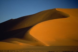 LIBYA , South West, Achan , Orange desert sand dunes partially cast in shadow against a clear blue