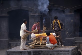NEPAL, Kathmandu, Cremation at Pashupatinath Temple.  Men gathered to light funeral pyre.
