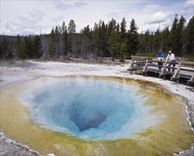 USA, Wyoming, Yellowstone, People looking into Morning Glory hot pool in the National Park.  Ochre