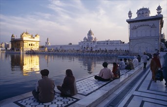 INDIA, Punjab, Amritsar, Golden Temple with pilgrims in low light with shimmering temple reflected